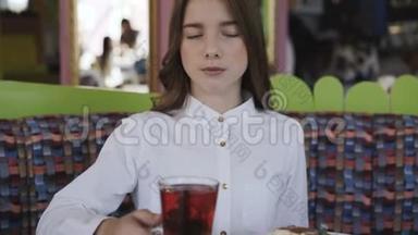 自信的年轻女孩在咖啡馆喝新鲜果汁的肖像。